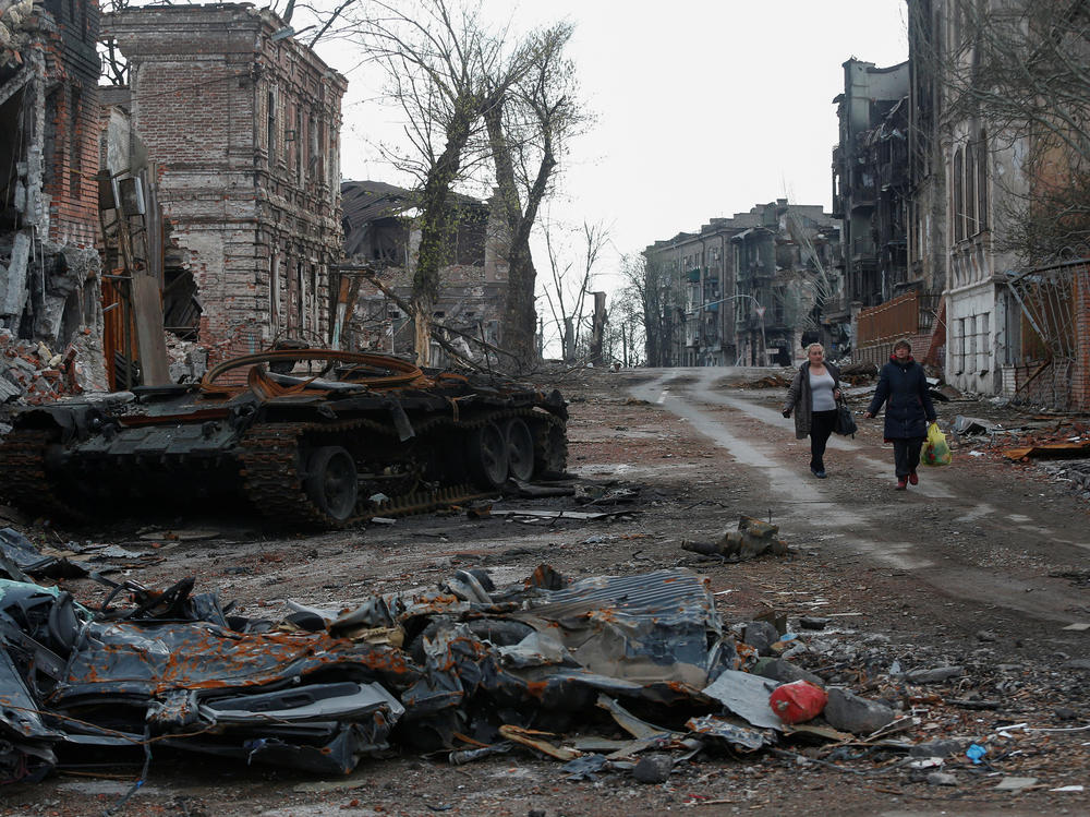 People walk near a destroyed tank and damaged buildings in the southern port city of Mariupol, Ukraine, on Friday.