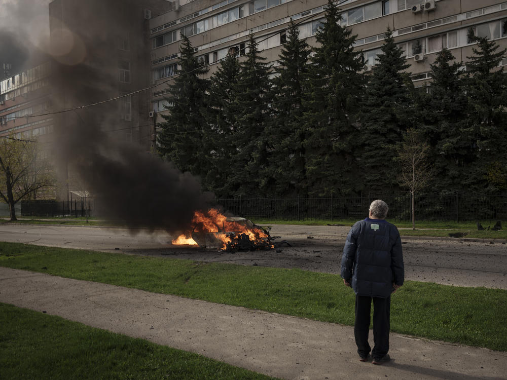 A man watches as a car burns with two people inside, after a Russian bombardment in Kharkiv, Ukraine, Thursday, April 21, 2022.