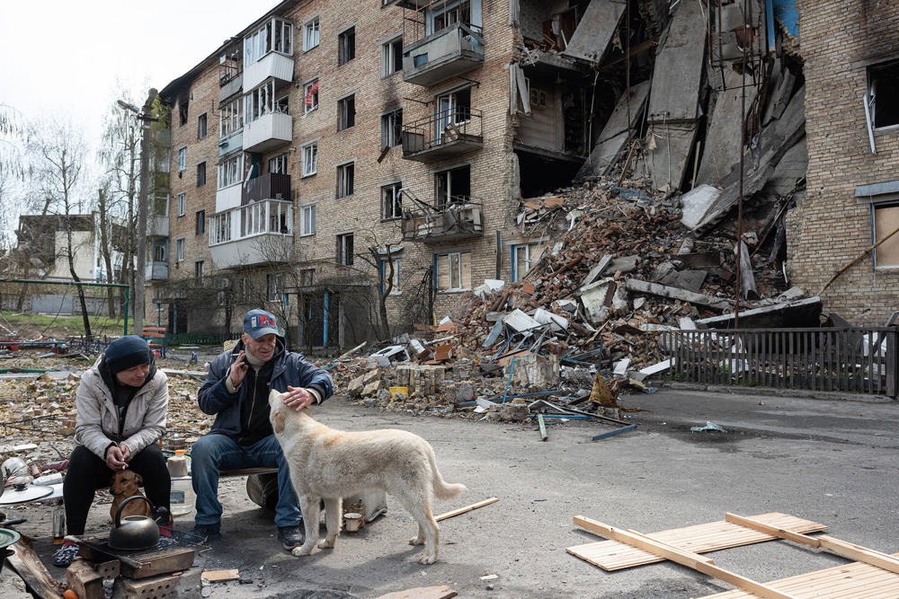 <strong>April 23:</strong> A man pets a dog by the makeshift stove in the courtyard of a heavily damaged apartment building in Horenka, Ukraine.