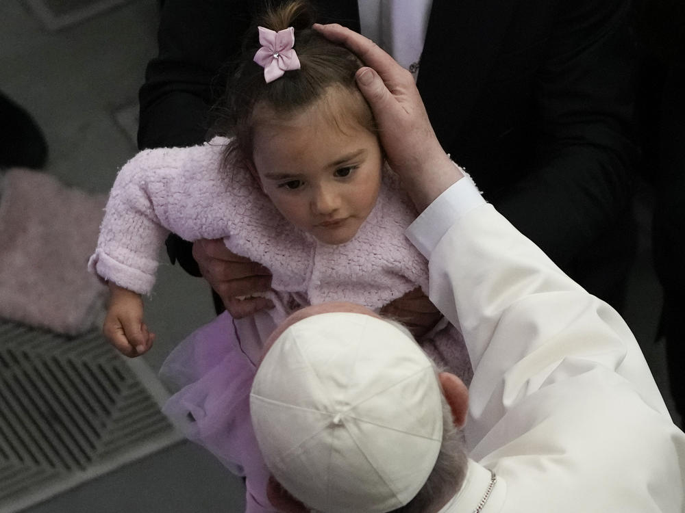 Pope Francis caresses a child in the Paul VI hall at the Vatican, Friday, April 8, 2022. Italy's Constitutional Court ruled that children should receive both parents' surnames at birth, not just the father's.