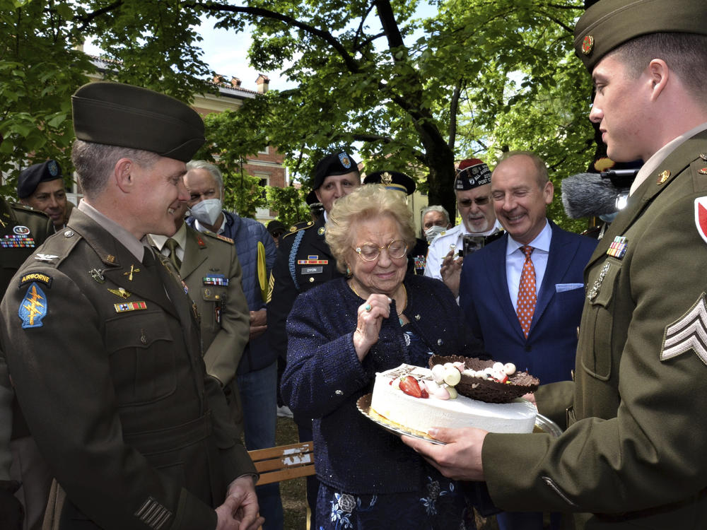 Soldiers from U.S. Army Garrison Italy return a birthday cake to Meri Mion, center, in Vicenza, northern Italy, Thursday, April 28, 2022, to replace the one U.S. soldiers ate as they entered her hometown during one of the final battles of World War II. Mion, who turns 90 on Friday, wiped away tears as she was presented with the cake.