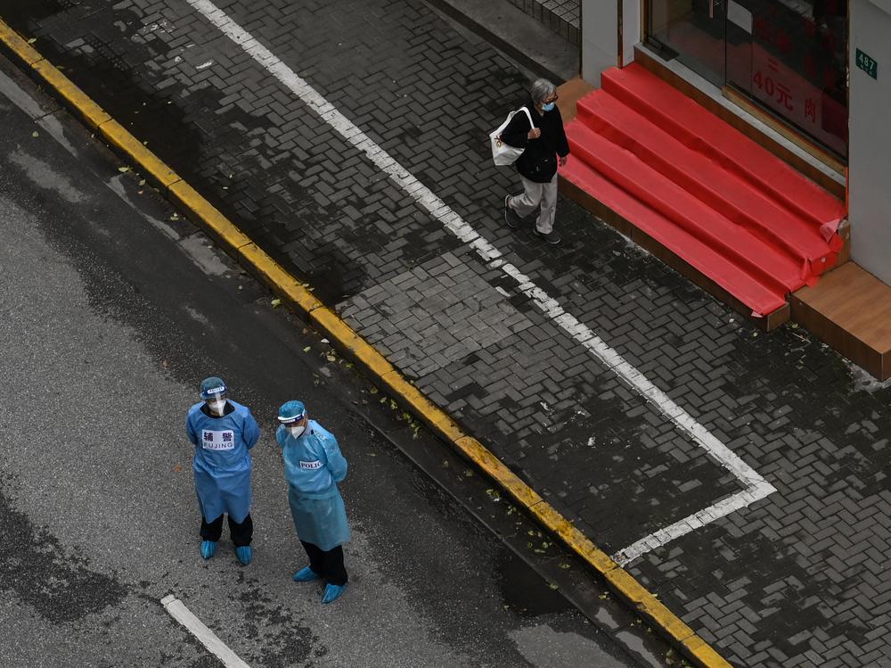 A resident walks on a street as policeman, right, and a police assistant, left, stand by during a COVID-19 lockdown in a district in Shanghai on April 29. China is shutting down factories and ports in a bid to contain a spread of COVID-19, raising concerns about global supply chains.