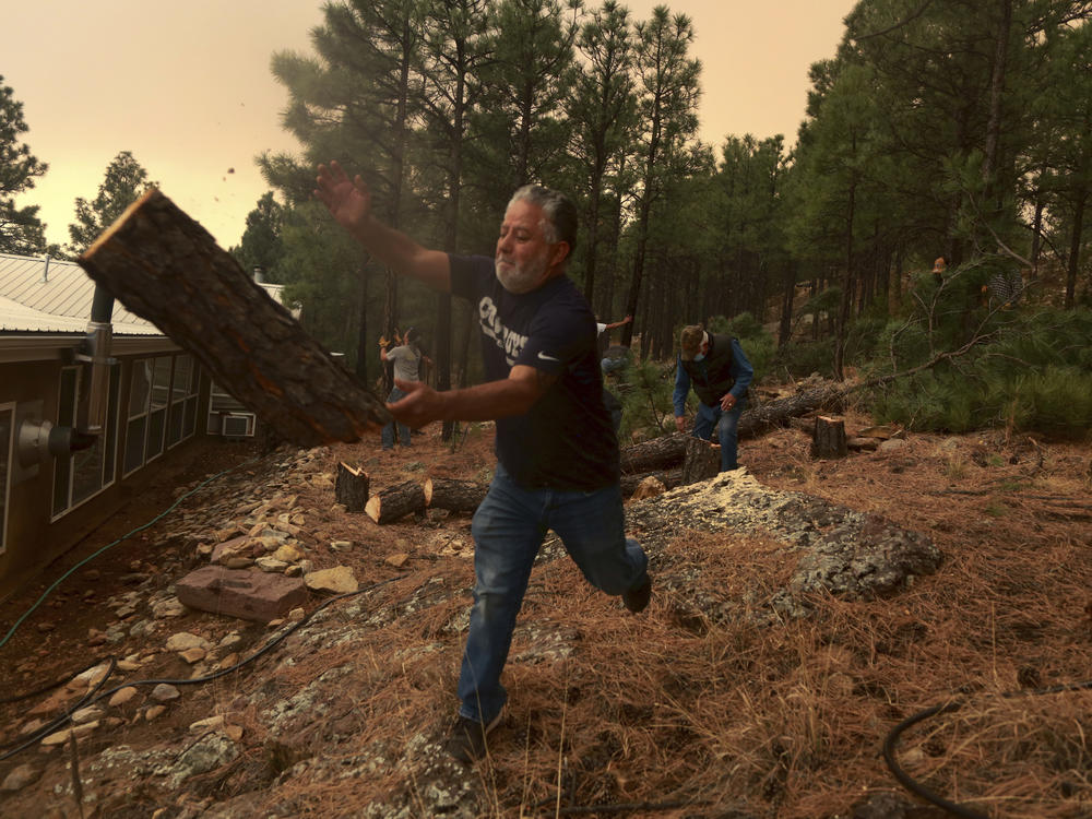 Chris Castillo throws a freshly cut log as he and his cousins clear a wireline along a family member's home in Las Vegas, N.M., on Monday. Wind-whipped flames are marching across more of New Mexico's tinder-dry mountainsides, forcing the evacuation of area residents.