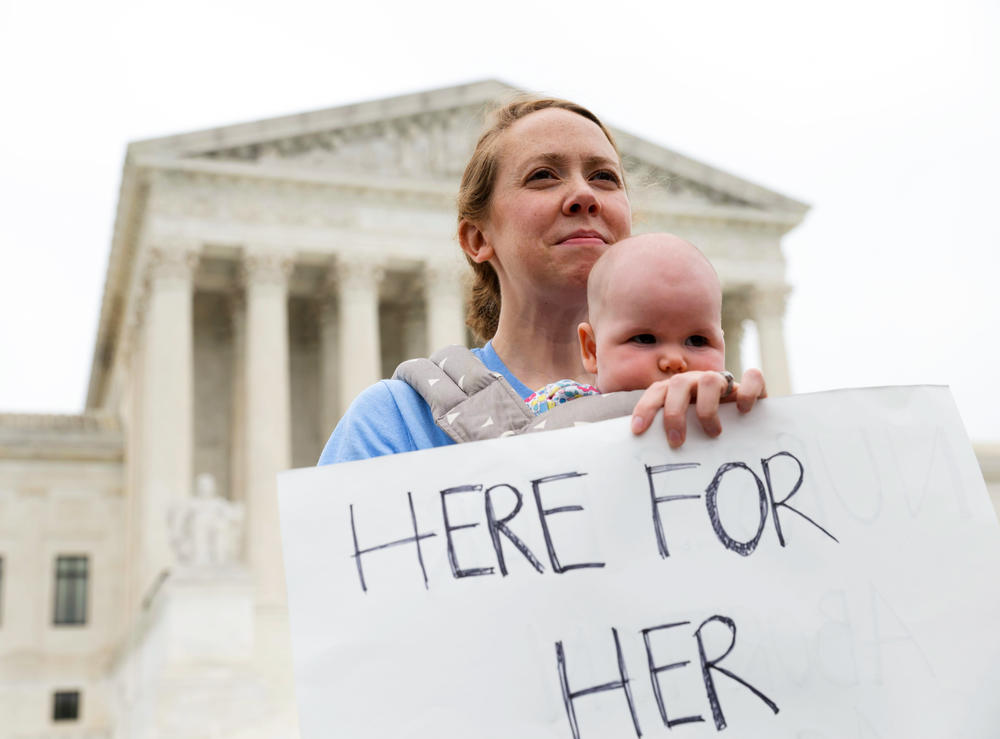 Zoe Gandee holds her 4-month-old daughter, Matilda Gandee-Riggs, with a sign that reads 