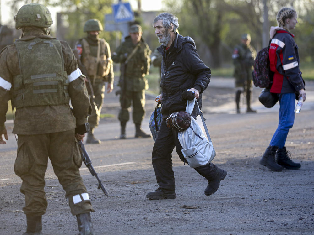 A man who left a shelter in the Azovstal steel plant in Mariupol walks to a bus between Russian army servicemen and Donetsk People's Republic militia on Friday.