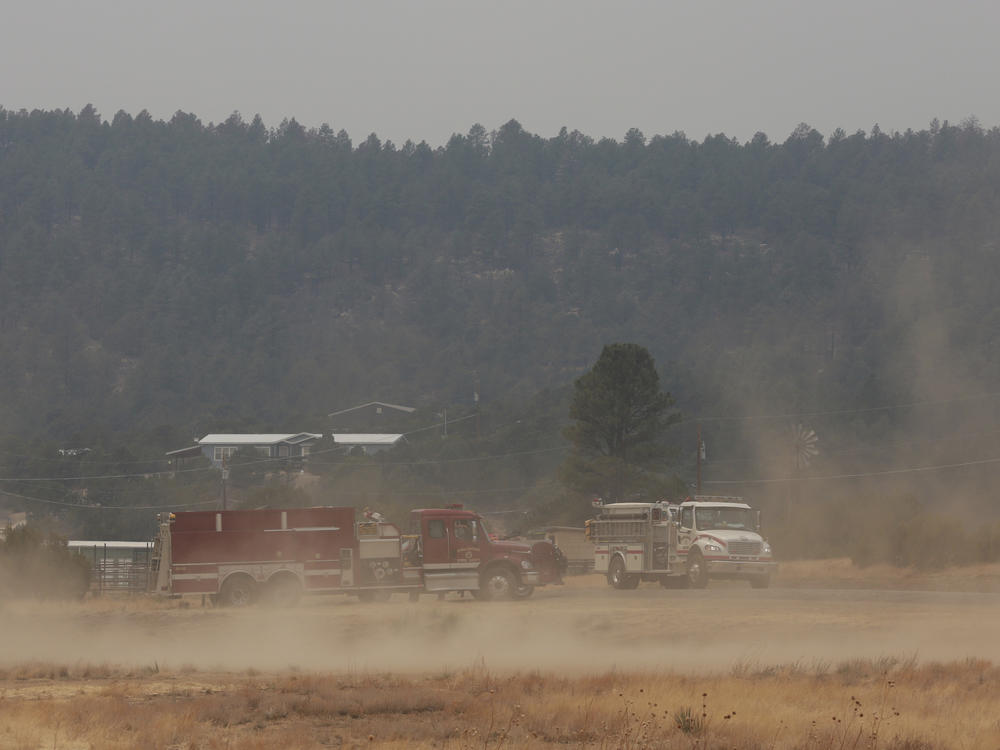 Wind kicks up dust at the fairgrounds as firefighters meet and confer about the wildfire raging on the other side of the hill behind them just outside of Las Vegas, N.M., on Saturday, May 7, 2022.