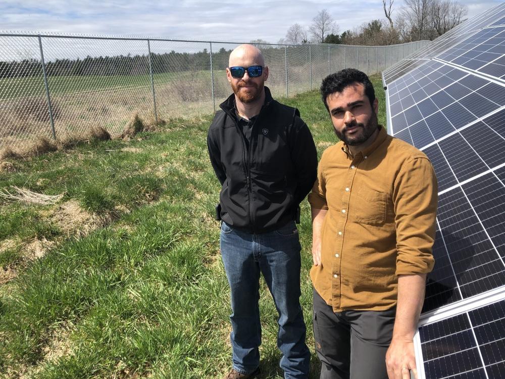 Adam Farkes and Leo Azevedo of BNRG at a solar energy project in Augusta, Maine. A bigger project planned on the far side of the fence is on hold because of a federal trade investigation.