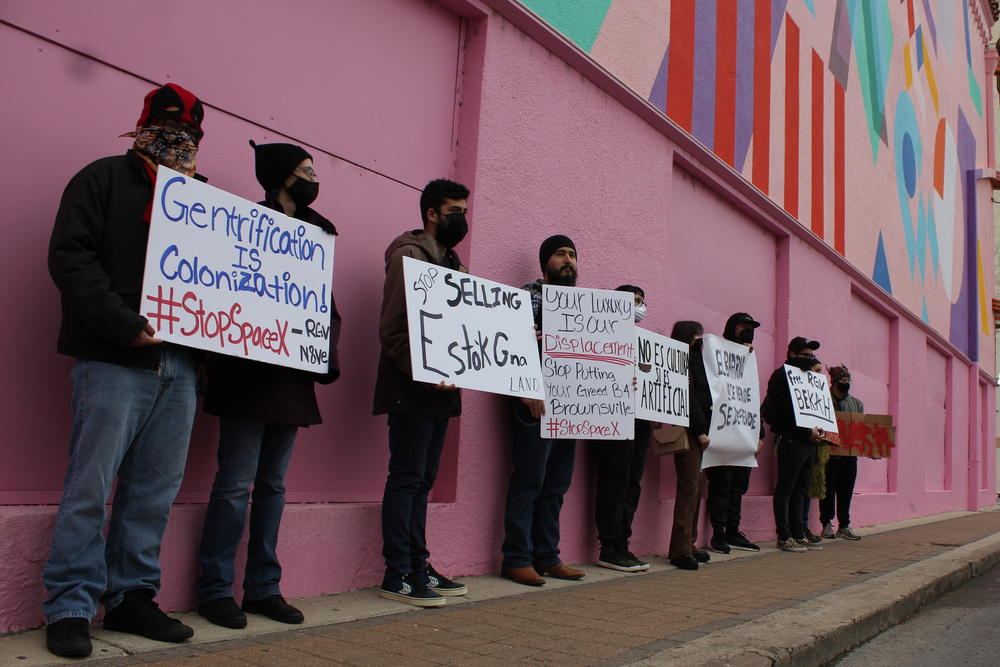 Local organizers protest Bekah Hinojosa's arrest for allegedly spraying graffiti below an Elon Musk-funded mural in downtown Brownsville. The mural, on the side of the Capitol Theater, can be seen behind them.