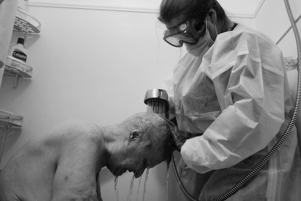 Kristi Stevens bathes patient Dick Barker in a stand-up shower in June of 2020. Personal protective equipment is a major emotional and psychological barrier for home health workers to adjust to, especially in caring for patients where touch is so vital to their care.