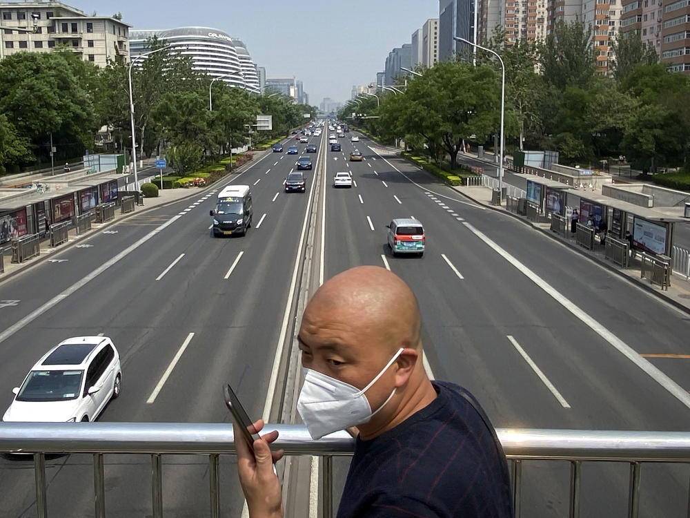 A man wearing a face mask stands on a bridge over an expressway in Beijing, Thursday, May 19, 2022. Parts of Beijing on Thursday halted daily mass testing that had been conducted over the past several weeks, but many testing sites remained busy due to requirements for a negative COVID test in the last 48 hours to enter some buildings in China's capital.