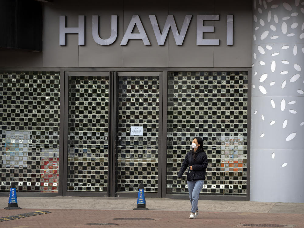 A woman wearing a face mask walks past a Huawei store temporarily closed due to coronavirus-related restrictions in Beijing, Thursday, May 12, 2022. China's leaders are struggling to reverse a deepening economic slump while keeping a 