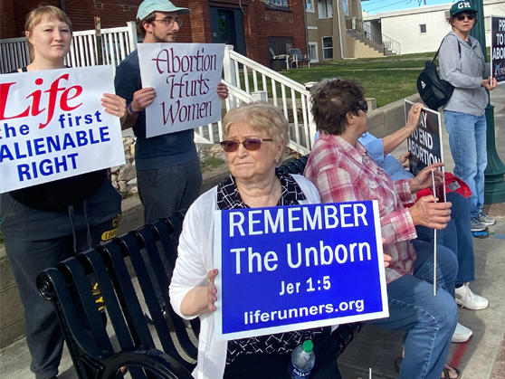(Left) More than 100 people have been attending weekly anti-abortion prayer vigils outside the site of a future Casper, Wyo., clinic offering abortion and other health care services. (Right) Abortion-rights supporter Rikki Hayes holds up a sign near the site of a Wellspring Health Access clinic.