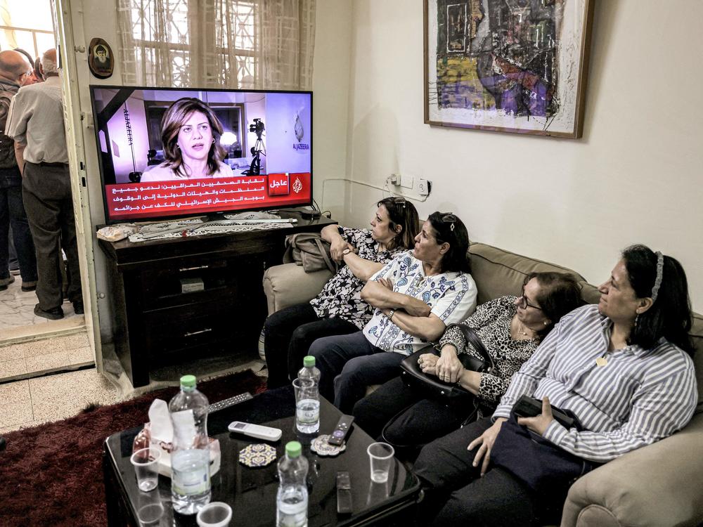 Women watch an Al Jazeera obituary report at the family home of journalist Shireen Abu Akleh after she was killed.
