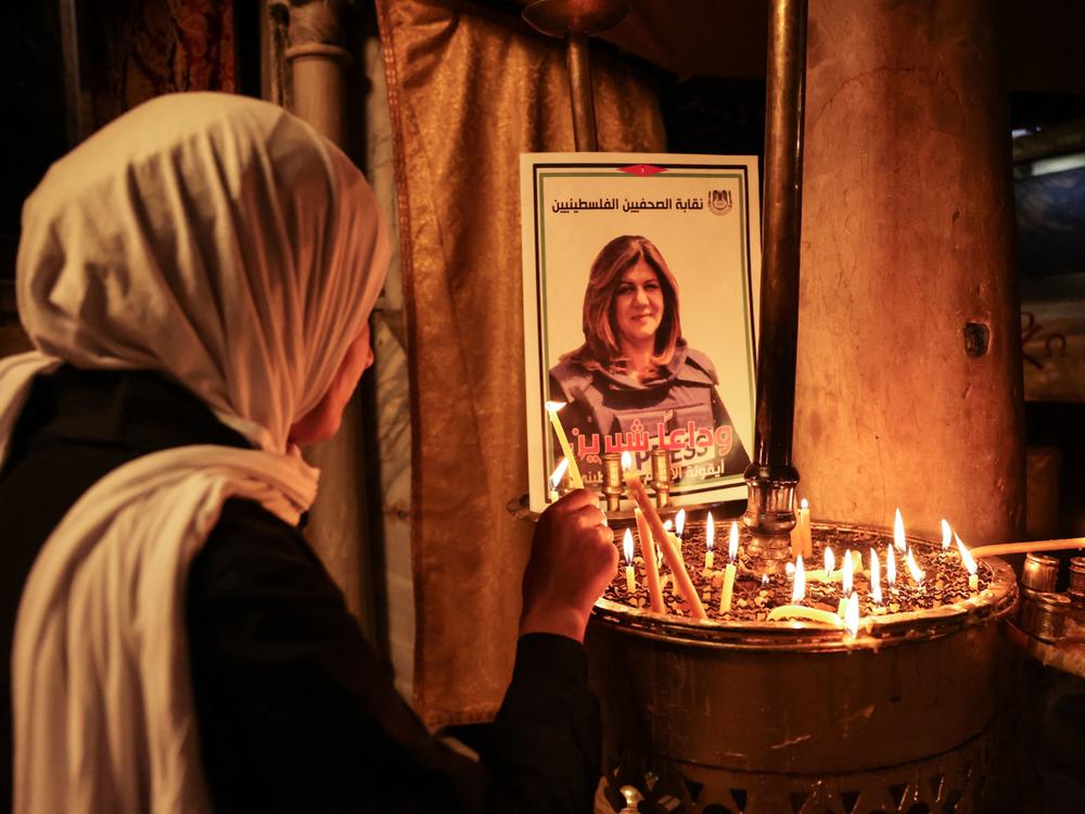 A woman lights a candle in front of a poster depicting Shireen Abu Akleh.