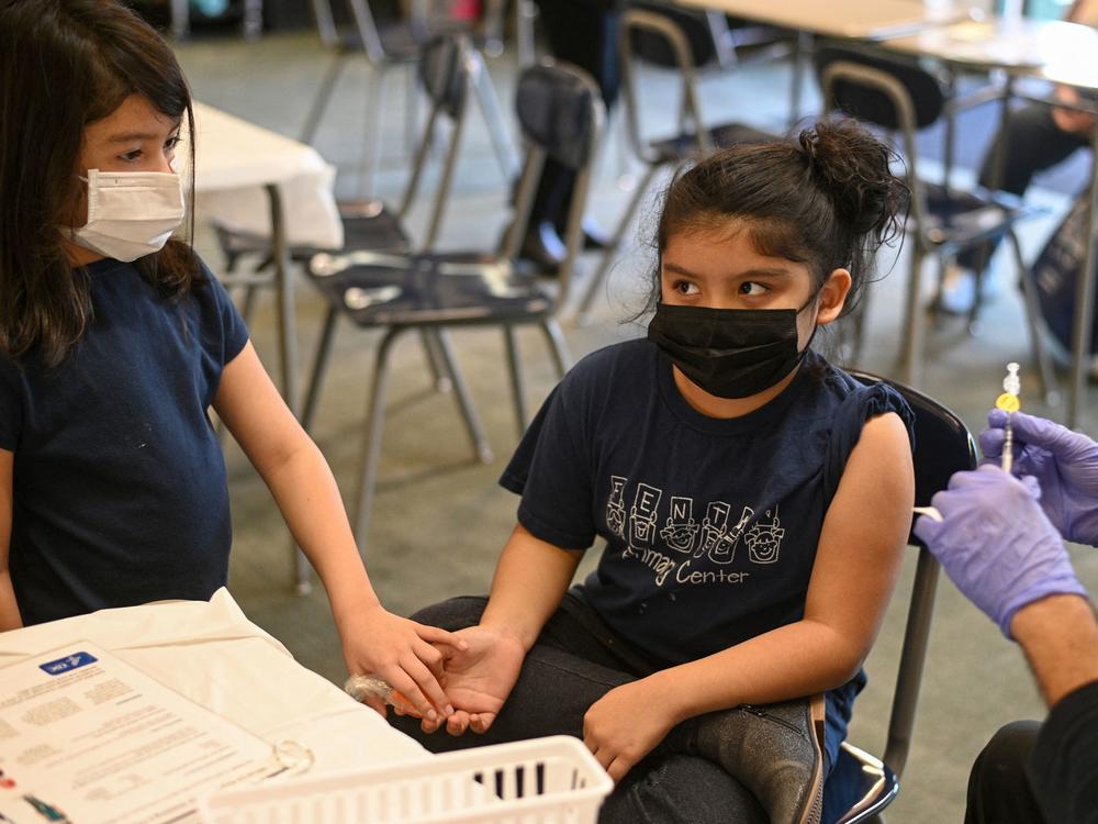 Pfizer will submit new data to the FDA this week about trials of its vaccine for kids younger than 5 years old. Here, a girl holds her sister's hand as a nurse prepares to administer the COVID-19 vaccine at a vaccination clinic in Los Angeles. Kids 5 and older have been eligible for the vaccine since last November.