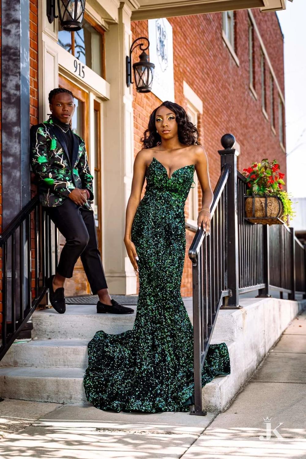 Emory James and Ayma Whitfield. Emory wore an embroidered black and green gold-trimmed suit. Instead of a button-down shirt, he chose a turtleneck. His shoes are black-studded, red-soled loafers.