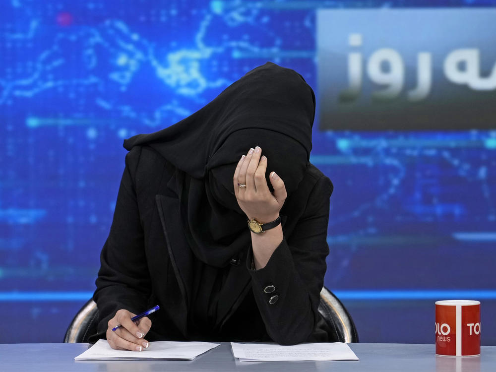 TV anchor Khatereh Ahmadi bows her head while wearing a face covering as she reads the news on TOLOnews, in Kabul, Afghanistan, on Sunday. The Taliban has started enforcing an order requiring female anchors to cover their faces while on air.