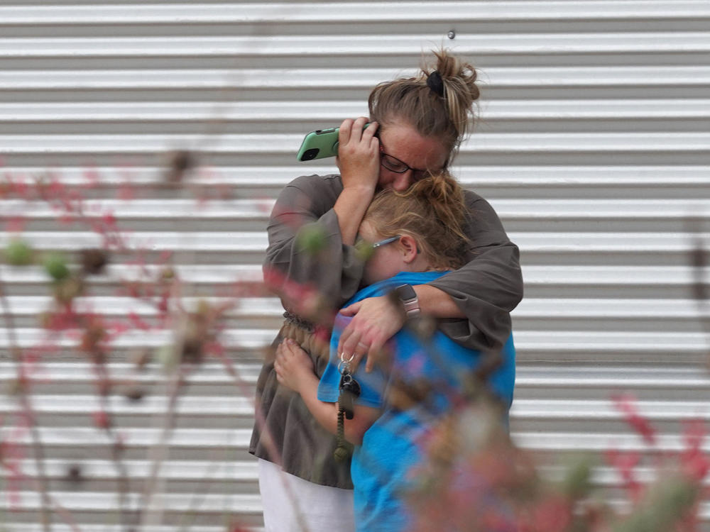 A woman cries and hugs a young girl while on the phone outside the Willie de Leon Civic Center where grief counseling will be offered in Uvalde, Texas.