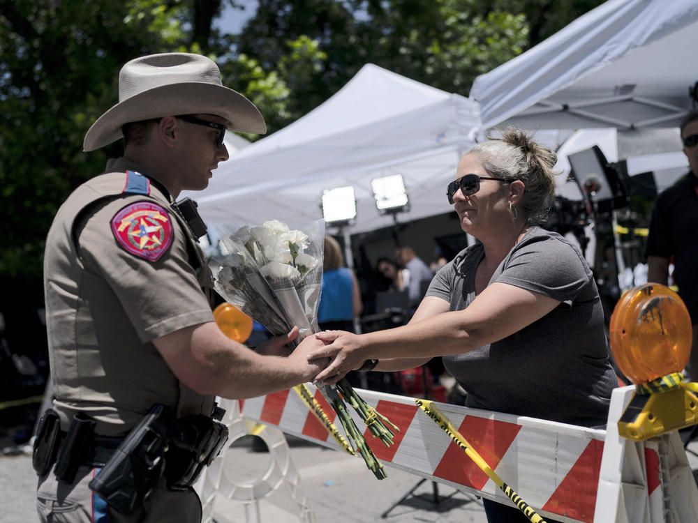 Sheena Rodriguez on Wednesday hands a state trooper a bouquet of flowers, honoring the victims killed in Tuesday's school shooting in Uvalde, Texas.