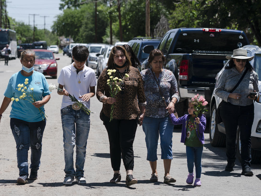 People walk with flowers to honor the victims in Tuesday's shooting at Robb Elementary School in Uvalde, Texas, Wednesday, May 25, 2022.
