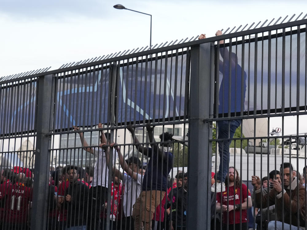 Fans climb on the fence in front of the Stade de France prior to the Champions League final soccer match between Liverpool and Real Madrid, in Saint Denis near Paris, Saturday, May 28, 2022.