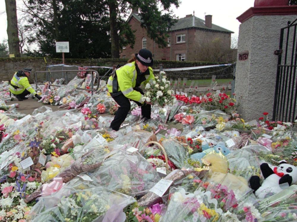 A police officer arranges bouquets of flowers in rows at a side entrance to Dunblane Primary School following a school shooting that left 16 students and one teacher dead.