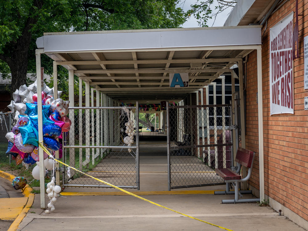 Balloons and caution tape are seen at the entrance to Robb Elementary School in Uvalde, Texas, on Tuesday. Investigators had initially said a teacher left a back door propped open at the school, but that account has now shifted.