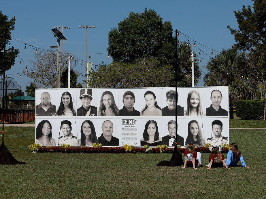 People sit Feb. 14 in front of a photo display of the 17 people killed four years earlier during a mass shooting at Marjory Stoneman Douglas High School in Parkland, Fla.