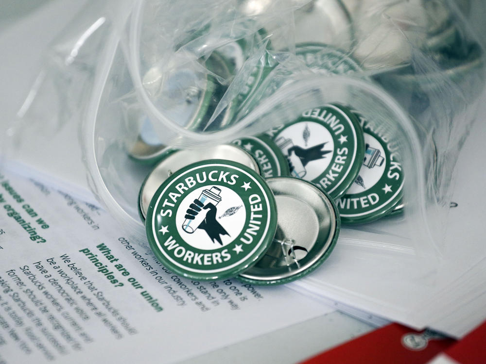 Pro-union pins sit on a table during a watch party for Starbucks' employees union election in December in Buffalo, N.Y. Starbucks union organizers say the company is closing a New York store to retaliate.