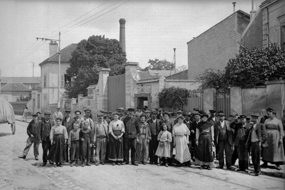 Workers stand at the exit of the Rattier factory in Bezons, France, circa 1905. Lunch pails became increasingly common at the workplace during that era in France.