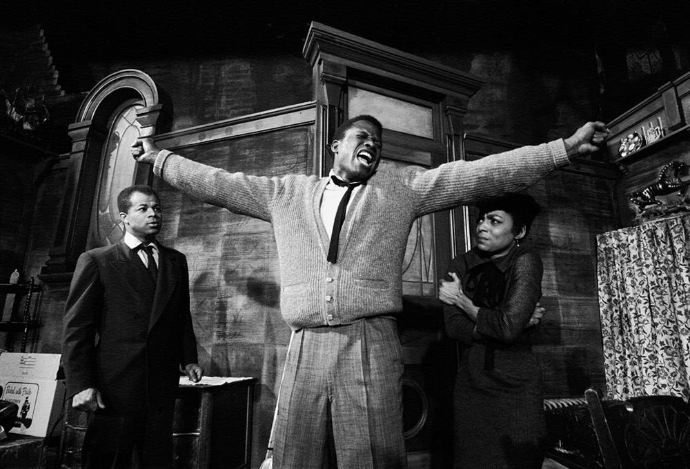 Sidney Poitier stands with arms outstretched in a dramatic scene from the play <em>A Raisin in the Sun</em>, with actor Ruby Dee visible on the right.