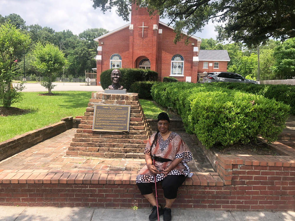 Descendant Vernetta Henson sits outside Union Baptist Church in Africatown. The church was started by Clotilda survivors in 1869. To her left is the bust of Cudjoe Lewis, one of Africatown's founders.