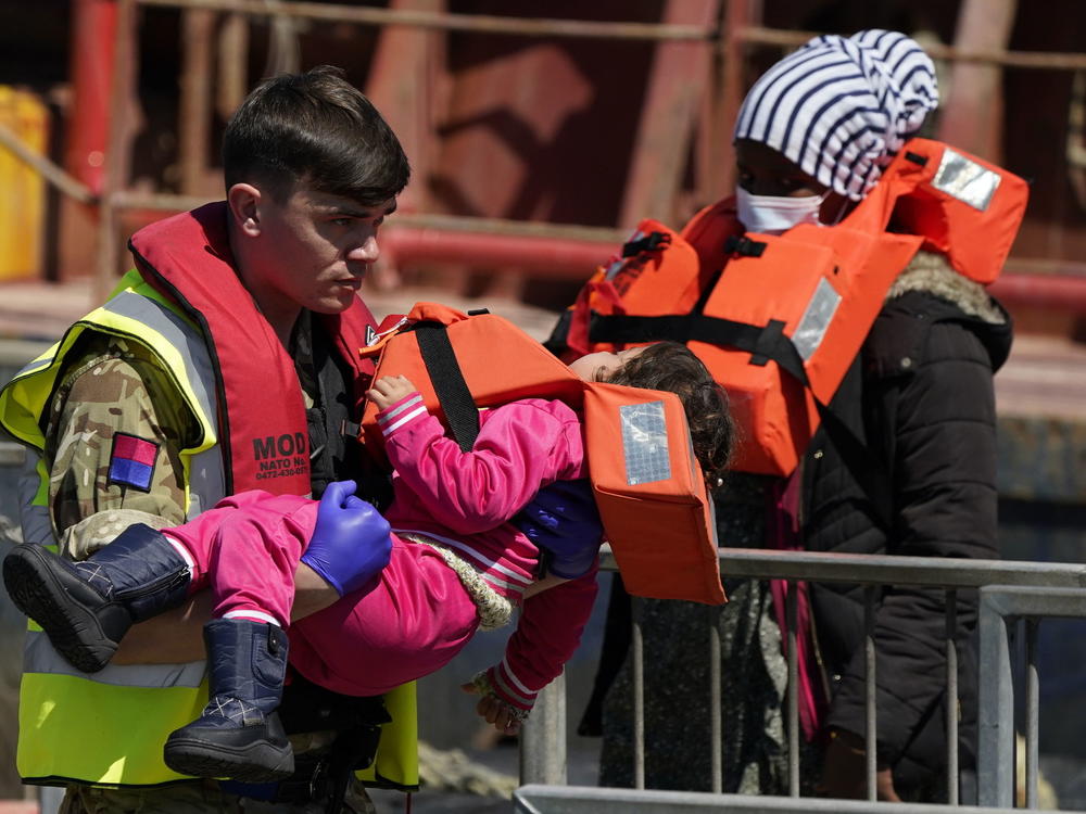 A soldier carries a child from a group of people thought to be migrants are brought in to Dover, England, by Border Force, following a small boat incident in the Channel, Tuesday June 14, 2022.