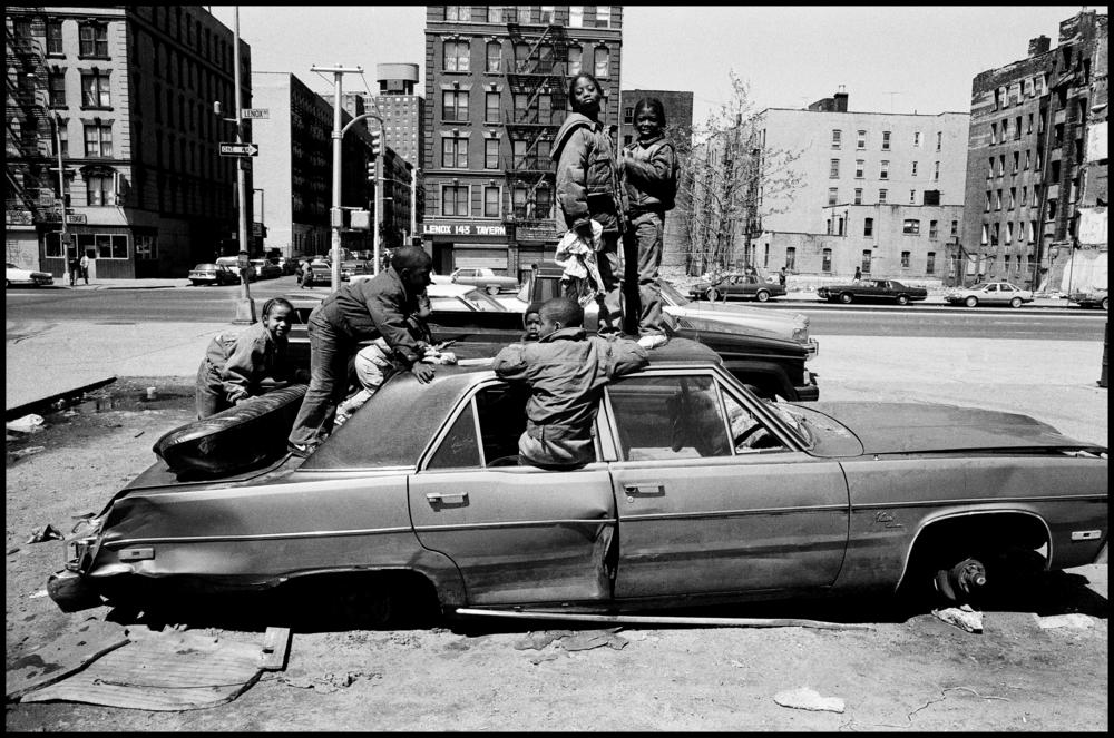 USA. New York City. 1987. Harlem street scene. Child playing in an abandoned car.