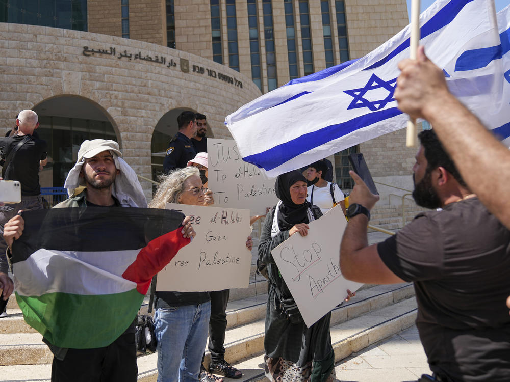 Supporters of Mohammed el-Halabi hold a Palestinian flag and placards as protesters wave Israeli flags, outside the district court in the southern Israeli city of Beersheba, Wednesday, June 15, 2022.