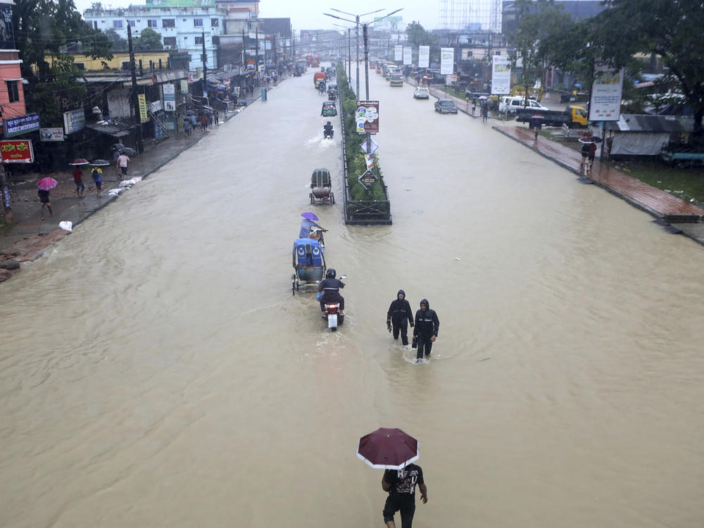 People wade through flooded waters in Sylhet, Bangladesh, Saturday, June 18, 2022. At least 18 people have died as floods cut a swatch across northeastern India and Bangladesh, leaving millions of homes underwater.