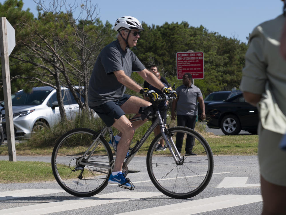 President Joe Biden pedals his bike towards a crowd at Gordons Pond in Rehoboth Beach, Del., Saturday. Biden fell from his bike as he tried to get off it to greet the crowd.