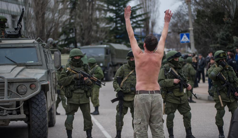 A Ukrainian man stands in protest in front of gunmen in unmarked uniforms in Ukraine's Crimean Peninsula in 2014. The forces were part of Russia's military, which remains in Crimea to this day.