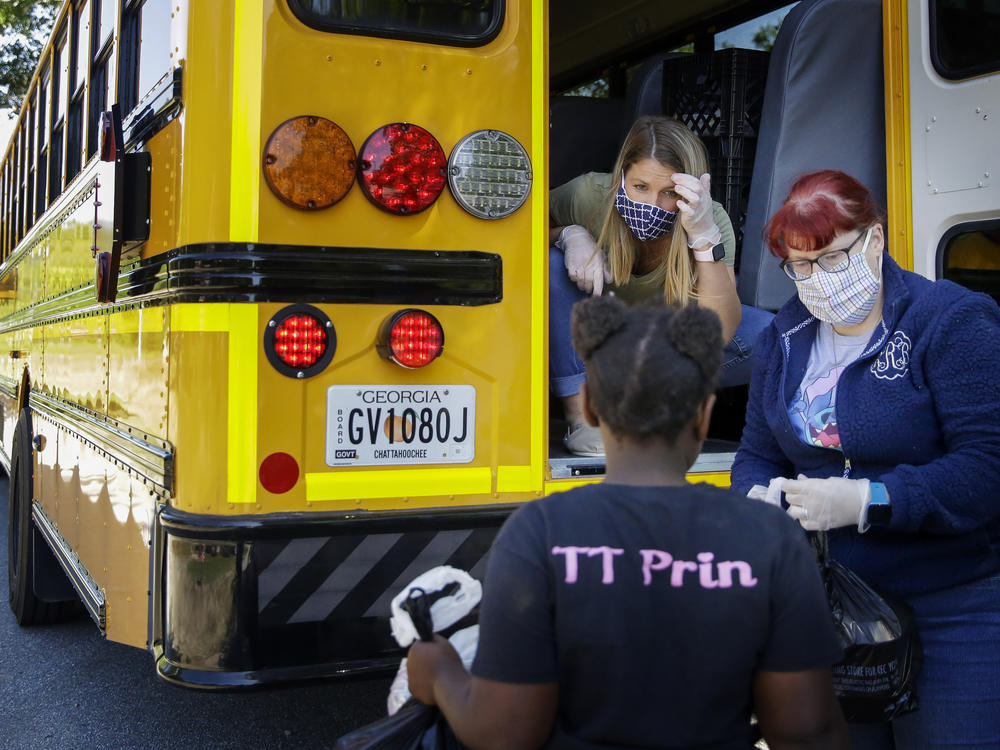 Teachers, Jennifer Scandle, left, and Renee Roberts, right, hand out a lunch to Kelsi Clarke, center, from a school bus.