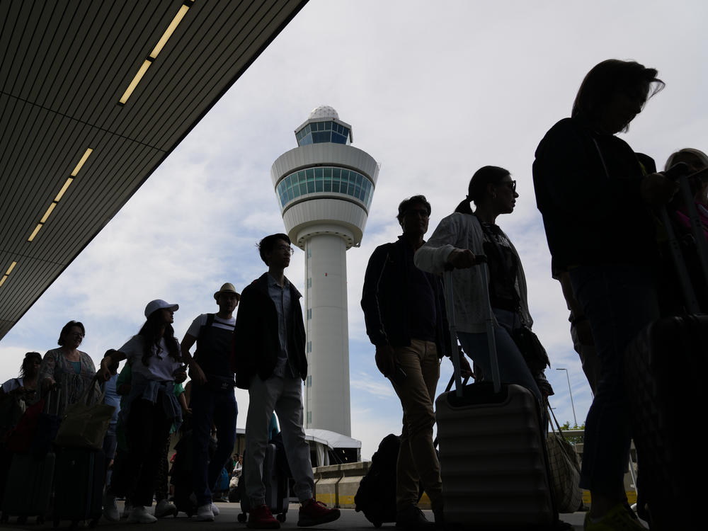 Travelers wait in long lines outside the terminal building to check in and board flights at Amsterdam's Schiphol Airport, Netherlands, Tuesday, June 21, 2022.