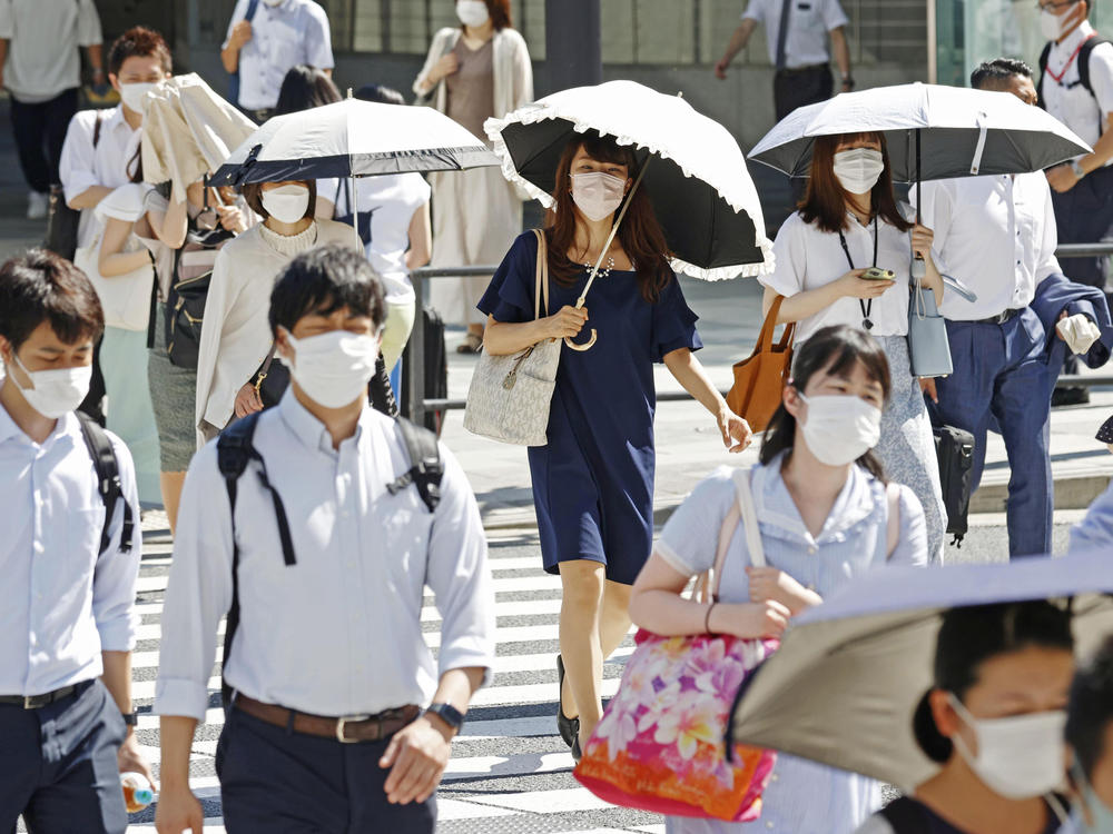 People, some of them holding parasols, cross an intersection amid heat, in Tokyo, Monday, June 27, 2022.