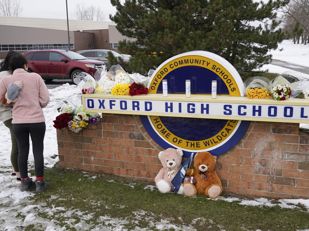 Students stand outside Oxford High School, near memorial items that were placed after the November 2021 shooting that took place at the Michigan school.