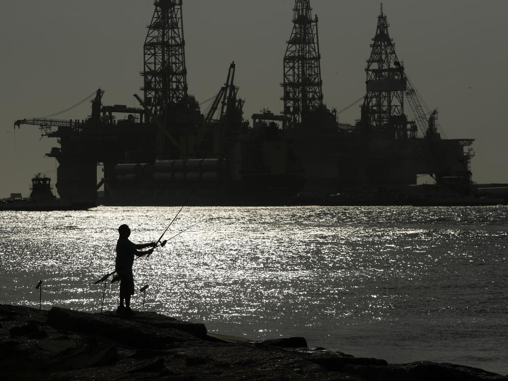 A man wears a face mark as he fishes near docked oil drilling platforms, Friday, May 8, 2020, in Port Aransas, Texas.
