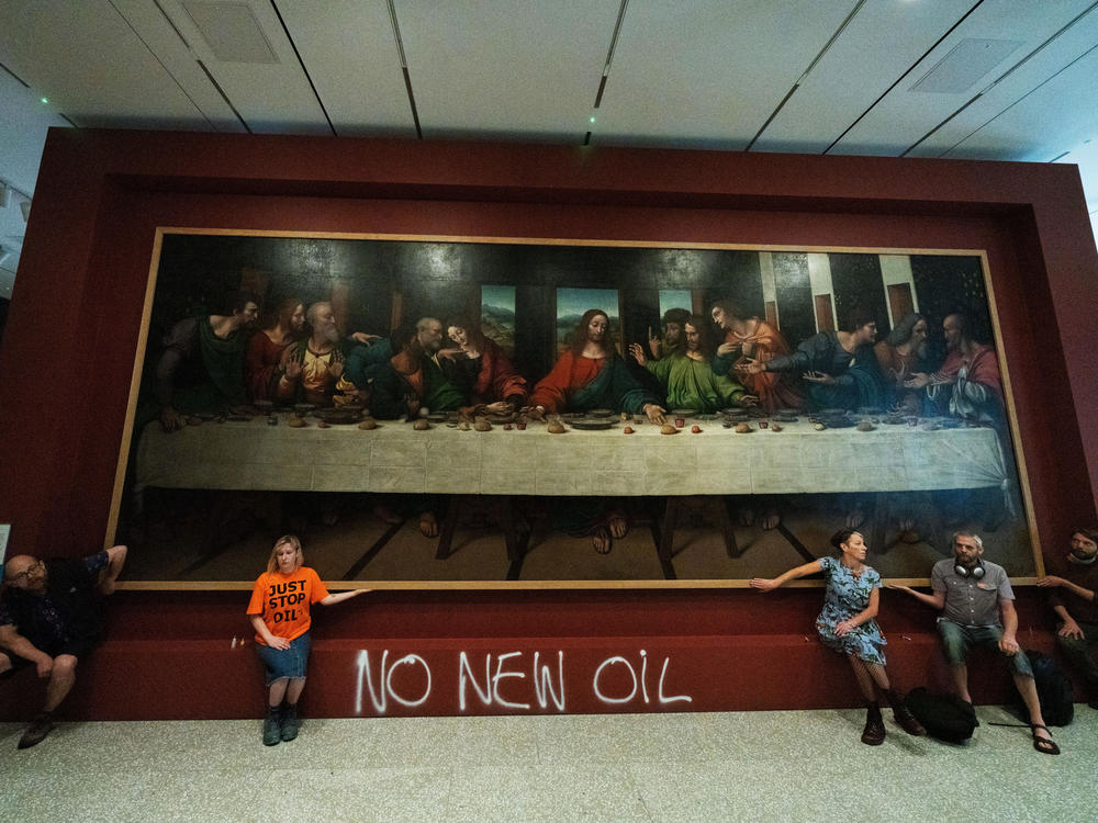 Five Just Stop Oil activists spray paint the wall and glue themselves to the frame of the painting <em>The Last Supper</em> on Tuesday at the Royal Academy in London.