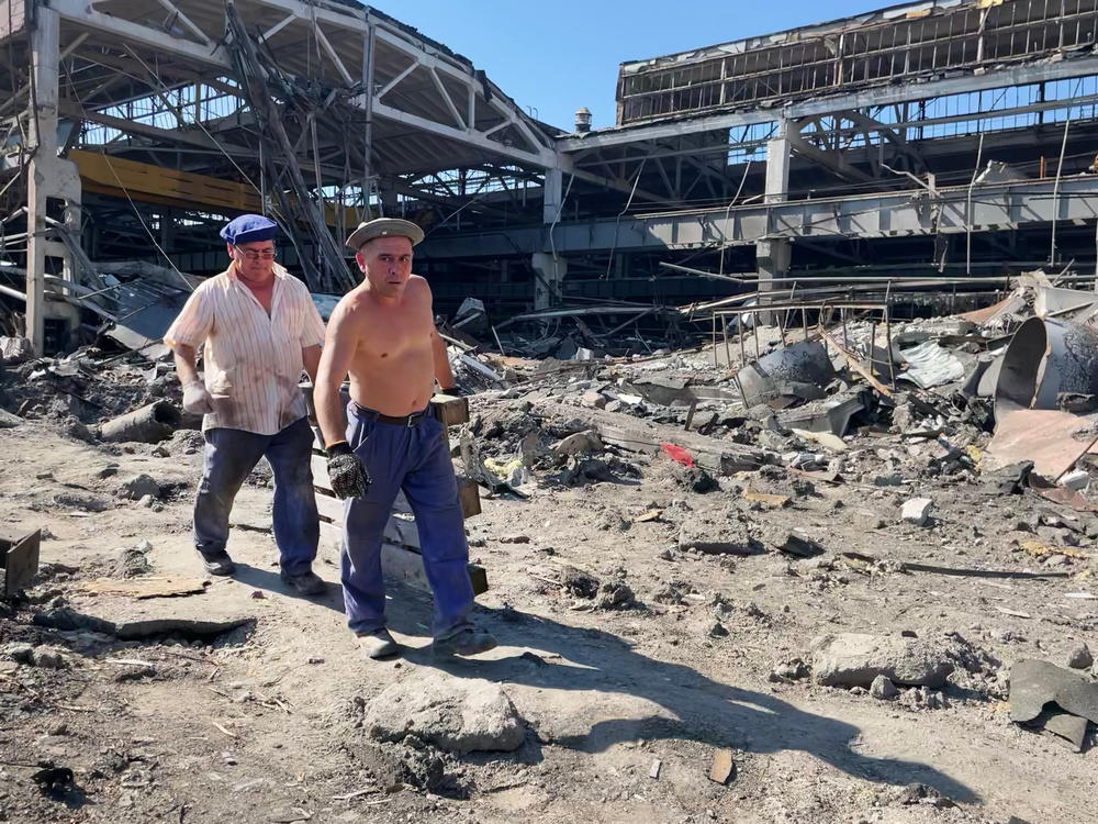 Workers at the Kredmash factory walk past the portion of the plant that was hit by a missile that landed moments after a missile hit a nearby shopping mall.