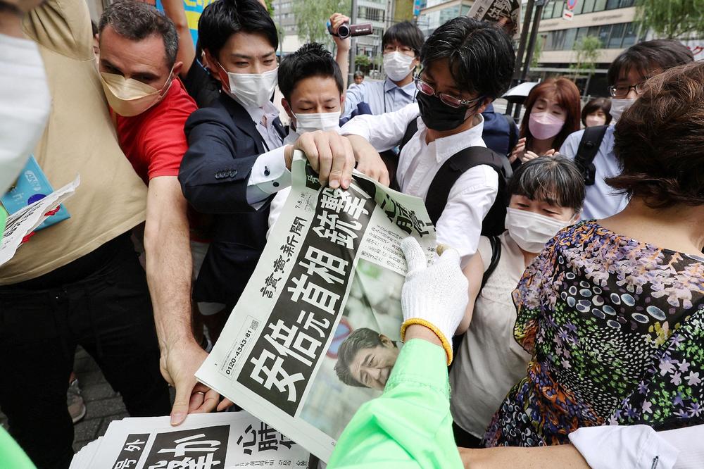 People crowd around to pick up an extra addition of a newspaper reporting the shooting of former Japanese Prime Minister Shinzo Abe along a street in Tokyo on Friday.