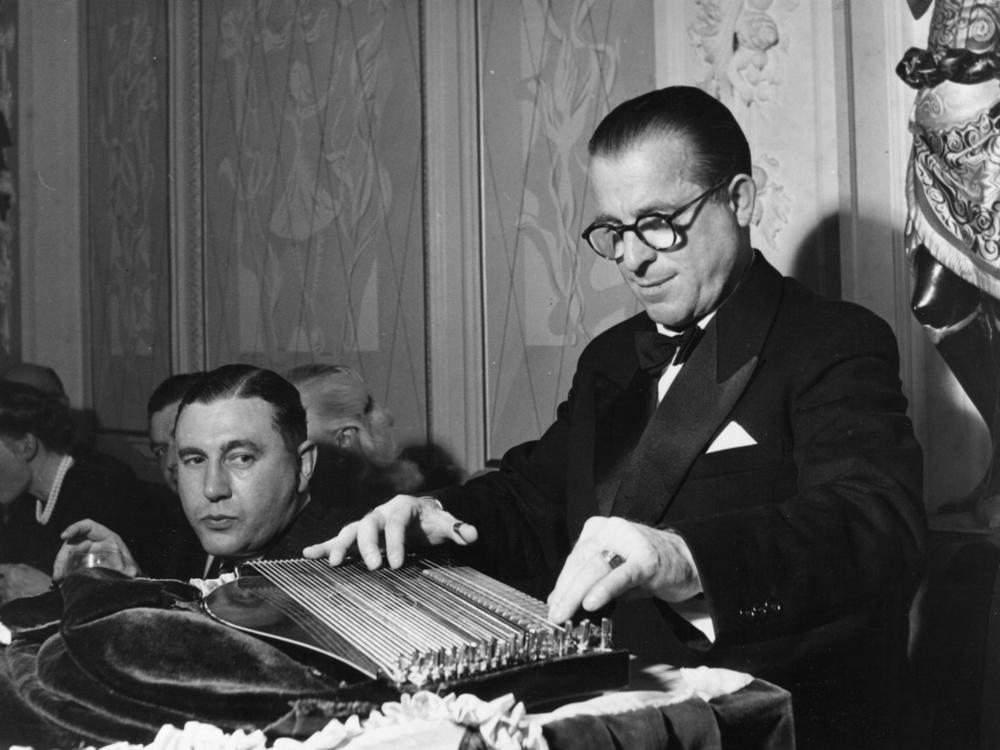 A guest at London's Empress Hotel in 1949 pauses to watch Anton Karas play the music he wrote for <em>The Third Man</em> on his zither.
