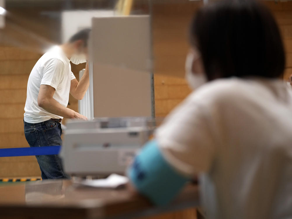 A staff member of a local election administration watches a voter preparing his ballot in the upper house elections at a polling station Sunday, July 10, 2022, in Tokyo.