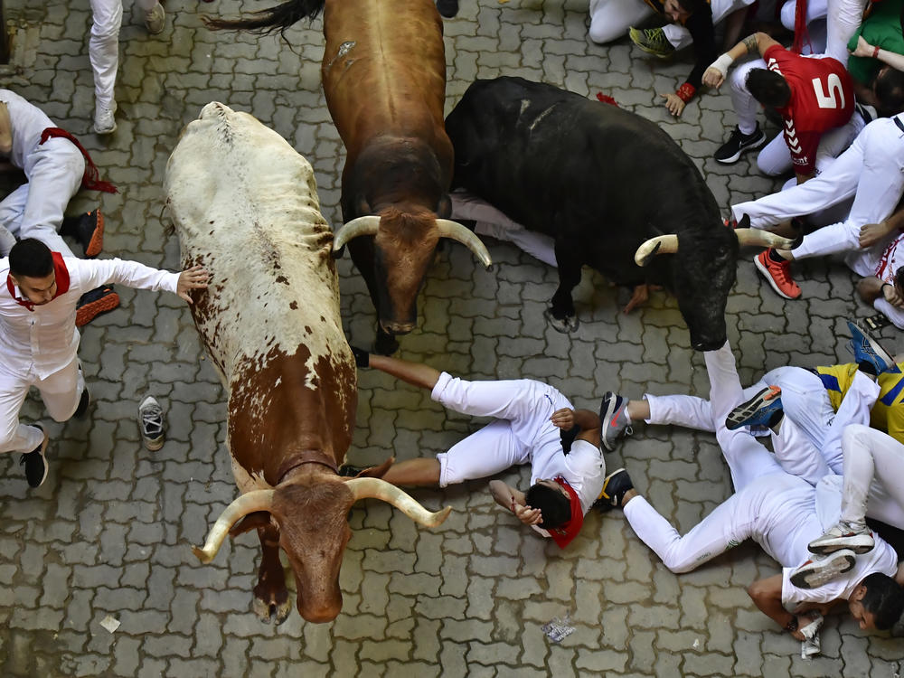 Runners fall during the running of the bulls at the San Fermin Festival in Pamplona, northern Spain, Monday, July 11, 2022.