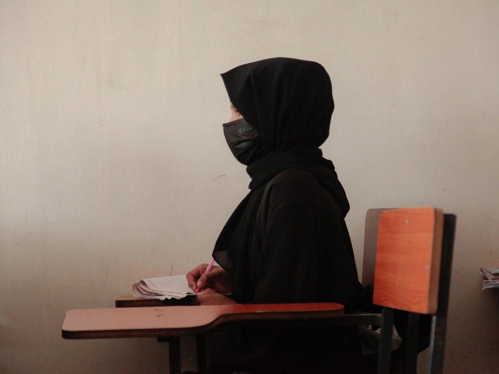 A teenage girl wearing a face mask, head scarf and long black robe listens to a math teacher at a tutoring center in Kabul. The center was established by a women's rights activist to circumvent a Taliban ban on girls attending secondary school. The activist said she has informal permission by Taliban authorities to run the center as long as teenage girls abide by a strict dress code.